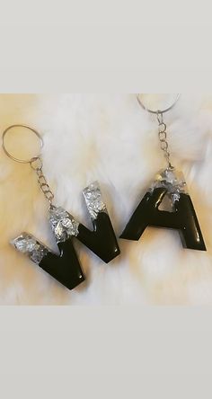 three black acrylic letters are hanging from a pair of silver metal earrings on a white fur background