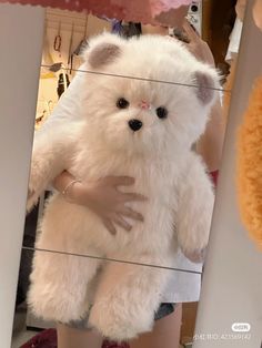 a person holding a large white teddy bear in front of a mirror with other stuffed animals behind it