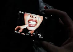 a person holding up a cell phone to take a photo with their teeth in the dark