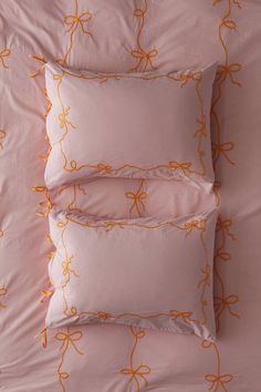 three pillows with orange bows on them sitting on top of a pink comforter covered bed