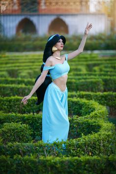 a woman in a blue dress is standing in a maze with her hand up to the sky