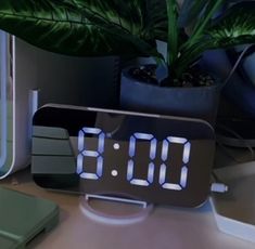 an alarm clock sitting on top of a desk next to a plant