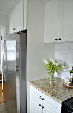 a kitchen with white cabinets and marble counter tops, stainless steel refrigerator and black stove