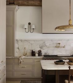 a kitchen with marble counter tops and gold accents on the cabinets, along with two hanging lights