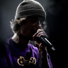 a man with tattoos on his arm and wearing a beanie singing into a microphone