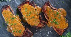 three steaks with sauce and herbs on a slate board