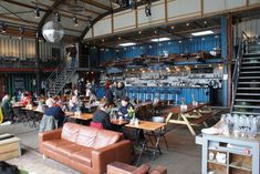 people are sitting at tables in a large warehouse like setting with blue shipping containers on the walls