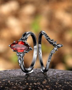 two wedding rings with red stone in the middle on top of a piece of rock