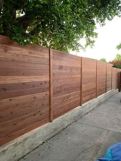 a bike parked next to a wooden fence in front of a tree on the sidewalk