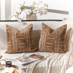 two decorative pillows sit on a couch next to a plate with cake and flowers in it