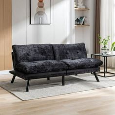 a black couch sitting on top of a hard wood floor next to a white rug