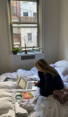 a woman is sitting on her bed looking at the laptop