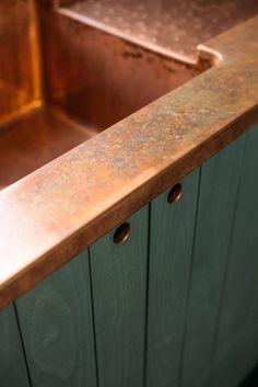 a wooden counter top sitting next to a metal sink in a kitchen with green cabinets