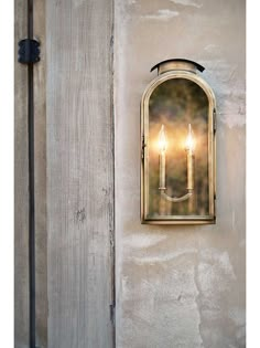 two lit candles are attached to the side of a wall mounted light on a building