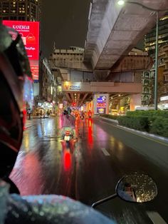 a person riding a motorcycle on a city street at night with lights reflecting off the wet pavement