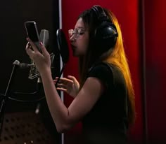 a woman wearing headphones and holding a cell phone in front of a recording microphone