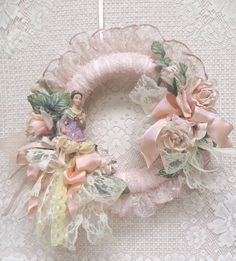 a pink wreath with angel figurines on top of it next to a lace doily