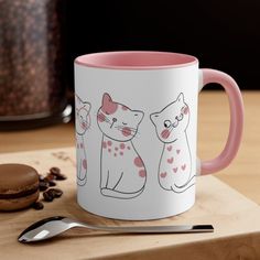 a pink and white coffee mug sitting on top of a wooden table next to a cookie