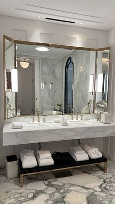 a bathroom with marble counter tops and gold framed mirrors on the wall, along with white folded towels