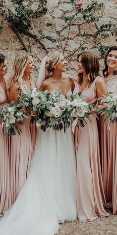 a group of women standing next to each other in front of a stone wall holding bouquets