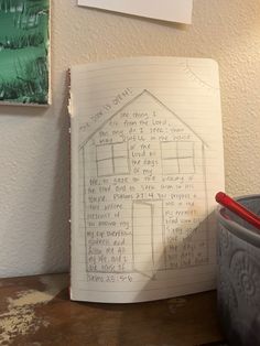 an open notebook with writing on it next to a trash can and a potted plant