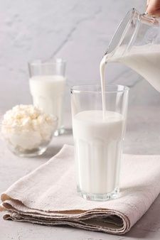 a person pouring milk into a glass on top of a napkin next to two glasses