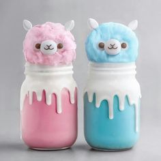 two little jars with some kind of stuff in them on a gray background, one is blue and the other is pink