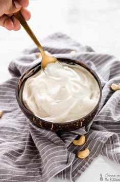 a hand holding a spoon over a bowl of whipped cream with peanuts on the side