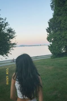 the back of a woman's head as she sits on grass near water and trees