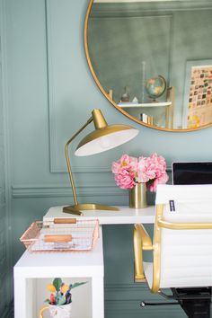 a white desk topped with a laptop computer next to a flower vase and a gold framed mirror