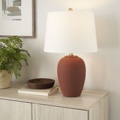 a table lamp sitting on top of a wooden dresser next to a potted plant