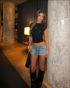 a beautiful young woman standing next to a tall pillar in front of a wall with her hand on her hip