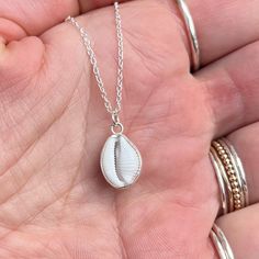 This beautiful necklace features an ethically sourced native cowrie shell in a custom made solid recycled silver wrapped setting with a silver chain.  Every necklace is handmade to order with the silver setting made custom for each shell, making each one unique.  This style 'wraps' the silver only around the edge of the shell holding it securely, whilst showing off both sides of the shell. There are two types of cowrie shell native to Cornwall, the European Cowrie ( Trivia monarcha ) and the Northern Cowrie ( Trivia arctica ).  The European cowrie is easily distinguishable from the Northern by the 3 dark spots on its shell and the fact it can grow to a larger size. I find many cowries whilst beach-combing in Cornwall and they are one of the small number of shells I use in my jewellery. Wit White Shell Charm Necklace Gift, White Shell Charm Necklace As Gift, White Shell Charm Necklace For Gift, White Sterling Silver Shell Necklace As Gift, White Sterling Silver Shell Necklace For Gift, Artisan Silver Necklaces For Beach, Handmade Silver Shell Pendant, White Sterling Silver Shell For Beach, Unique Silver Shell-shaped Necklace