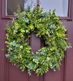 a wreath on the front door of a house with green leaves and greenery hanging from it