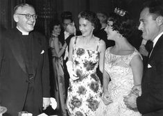 a group of people standing around each other at a formal event in black and white