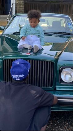 a little boy sitting on the hood of a green car