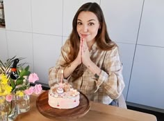 a woman sitting at a table with a cake in front of her and flowers behind her