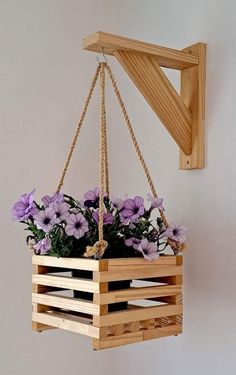 some purple flowers are in a wooden box hanging from a hook on a white wall