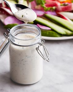 a spoon scooping dressing out of a glass jar next to a plate of vegetables