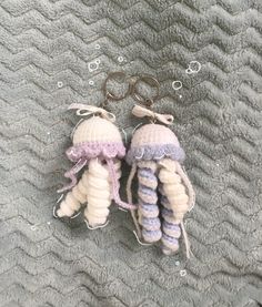 two crocheted jellyfish keychains are laying on a gray blanket with bubbles