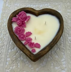 a candle in the shape of a heart with pink flowers on it sitting on a lace doily