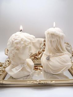 two white candles sitting on top of a golden tray next to each other with chains around them