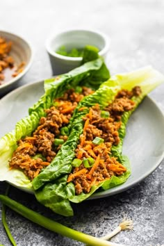 lettuce wraps filled with meat and vegetables on a plate next to dipping sauce