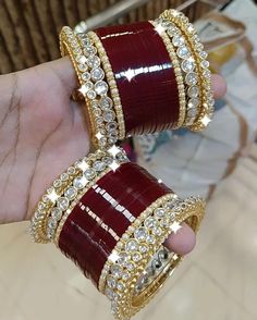 two red and gold bracelets are being held by someone's hand in a store