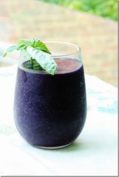 a glass filled with purple liquid sitting on top of a white table next to a green leaf