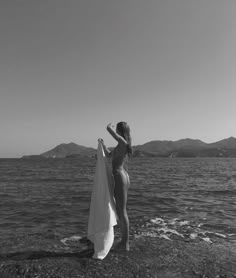 a woman is standing on the beach with her towel in hand and looking at the water