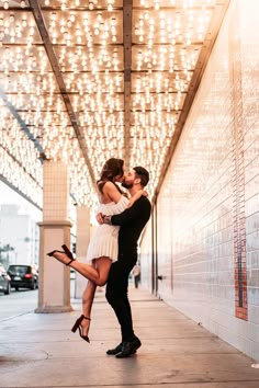 a man and woman kissing on the street under a canopy with lights in the background