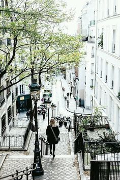 a woman walking down the stairs in an alleyway with trees and buildings on both sides