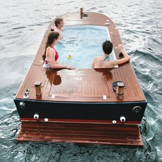 three people sitting on a boat in the middle of water with one person standing at the end