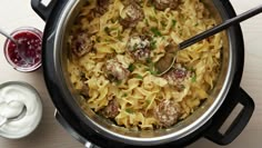 a pot filled with pasta and meatballs on top of a table next to sauce